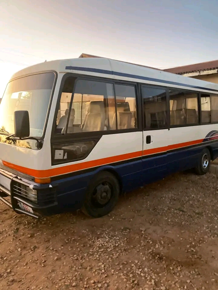 White and blue minibus with orange stripe parked on gravel at sunset