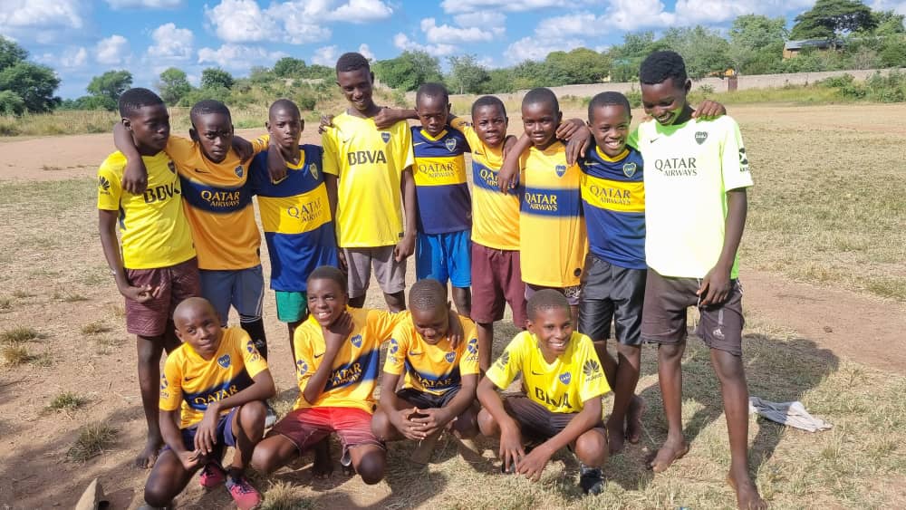 Group of African youth soccer players in Boca Juniors jerseys posing together on a dirt field