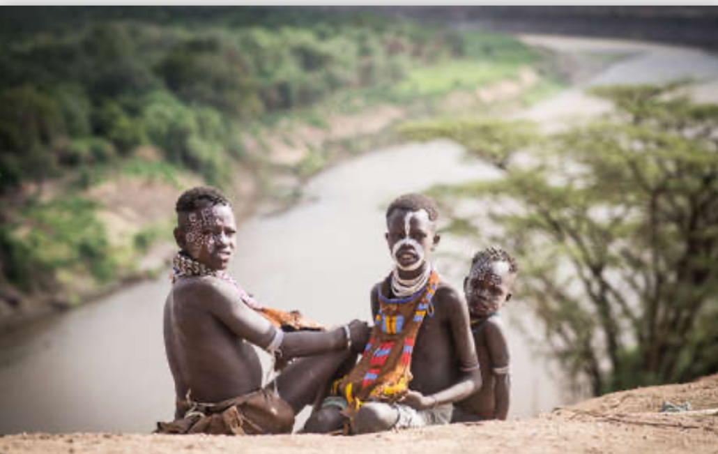 Three members of an African tribe with traditional body paint and jewelry sitting by a river