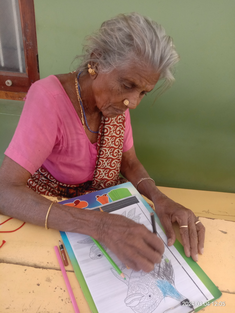 Elderly woman in pink sari coloring a fish illustration in a coloring book with colored pencils