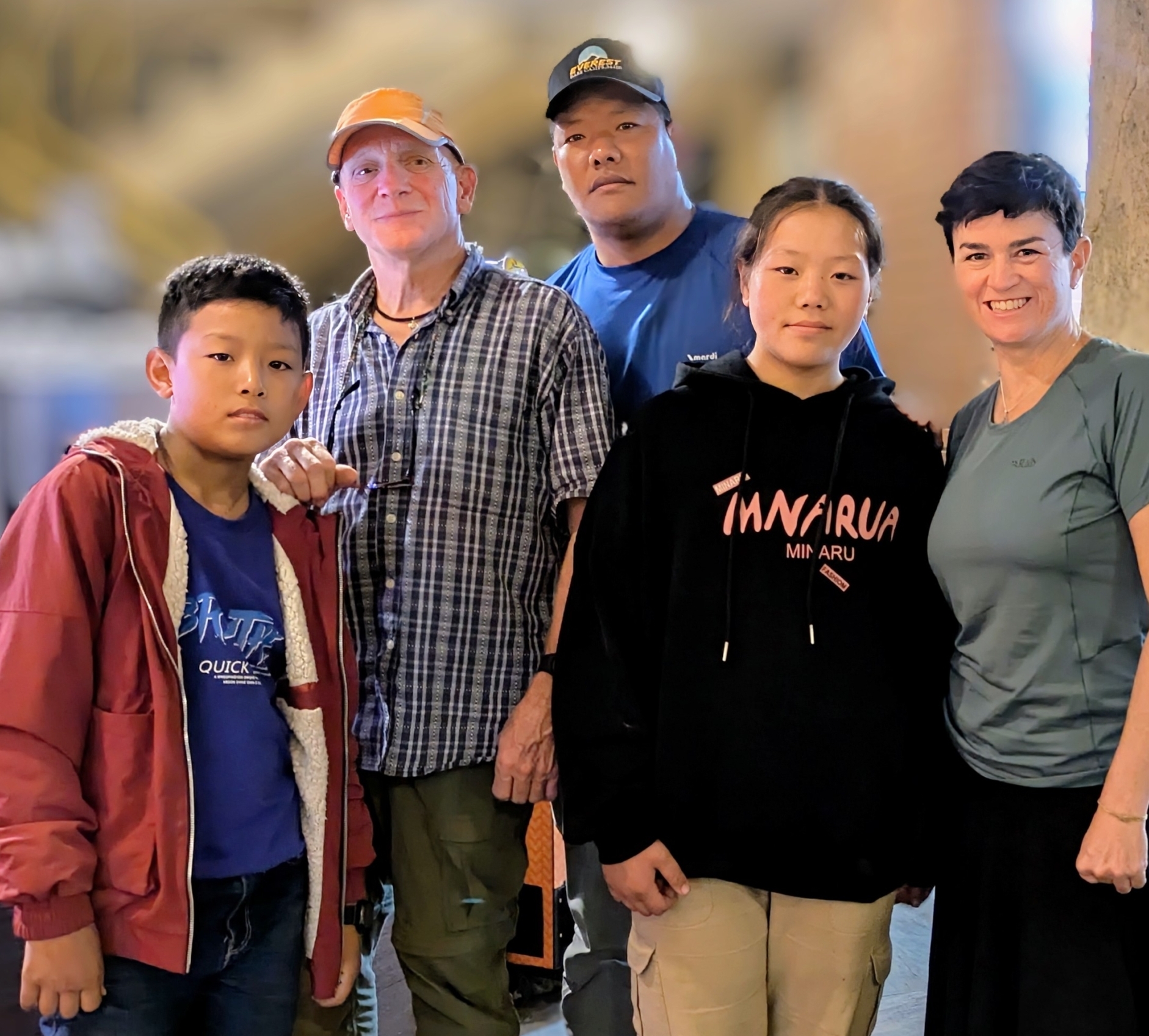 Five people posing together, including two children and three adults, with one man wearing an Everest cap