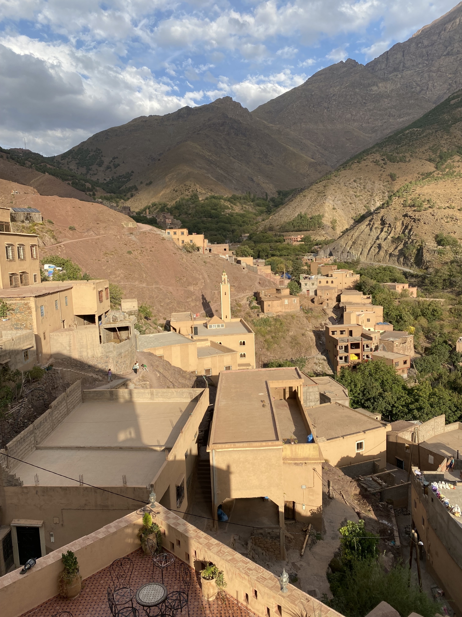 Moroccan mountain village with tan adobe buildings and a minaret nestled in the Atlas Mountains under cloudy skies