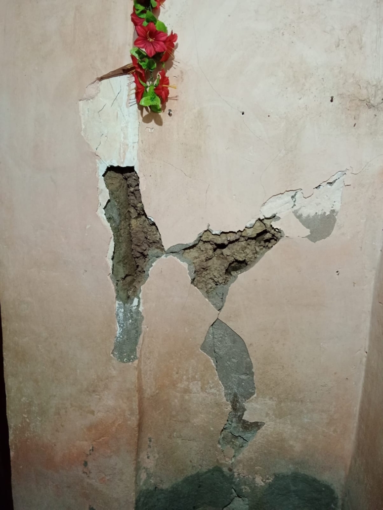 Severely cracked and damaged concrete wall with exposed inner layers, decorated with artificial red flowers and green leaves at top