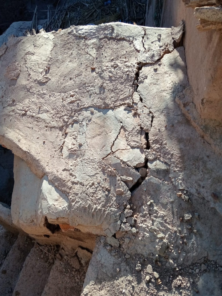 Cracked and weathered concrete or plaster wall with deep fissures and crumbling debris at the base