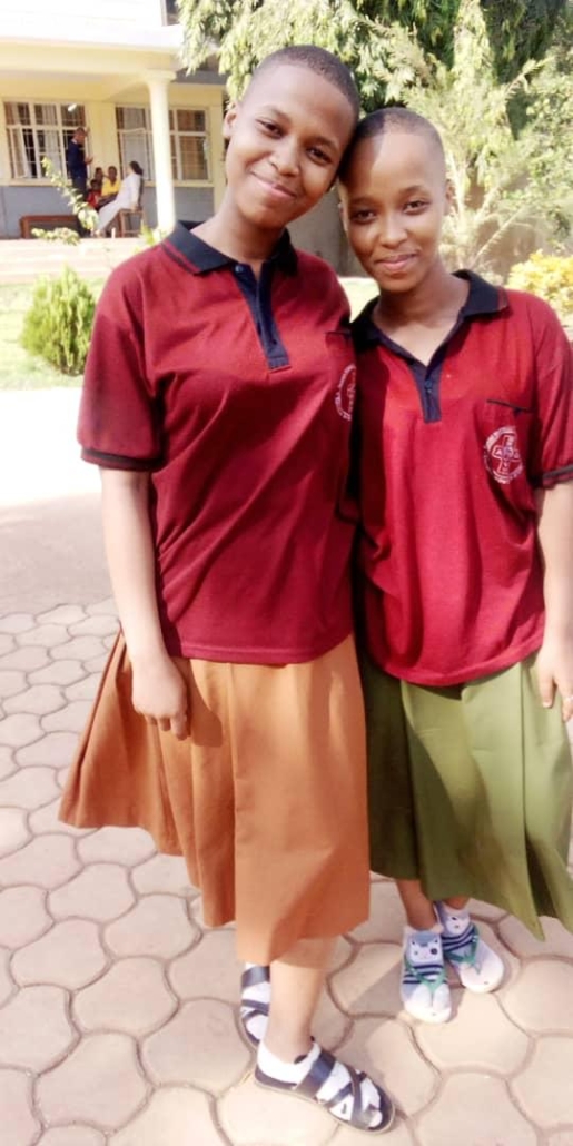 Two young women in matching red polo shirts with different colored skirts standing together and smiling on a paved walkway